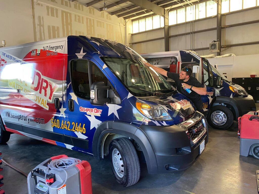 Semper Dry water removal van with patriotic wrap parked inside a warehouse, with a technician working beside it